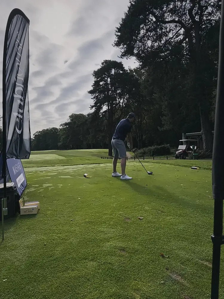 A player lining up his drive on a tee framed by tall pines