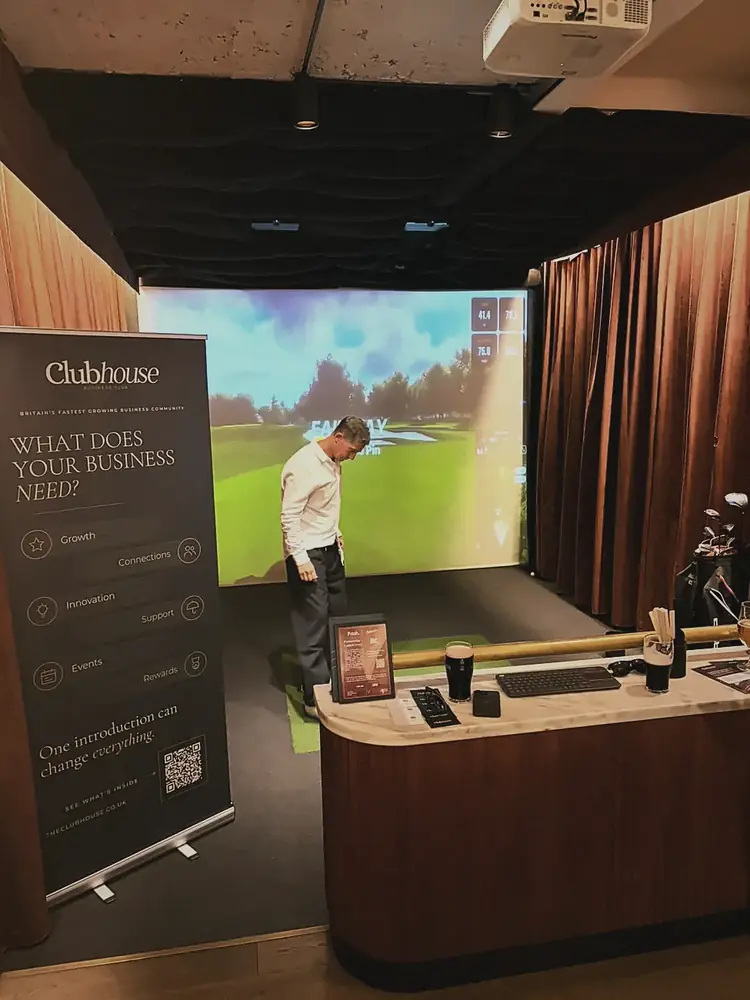 The Clubhouse banner beside a golf simulator bay at Pitch