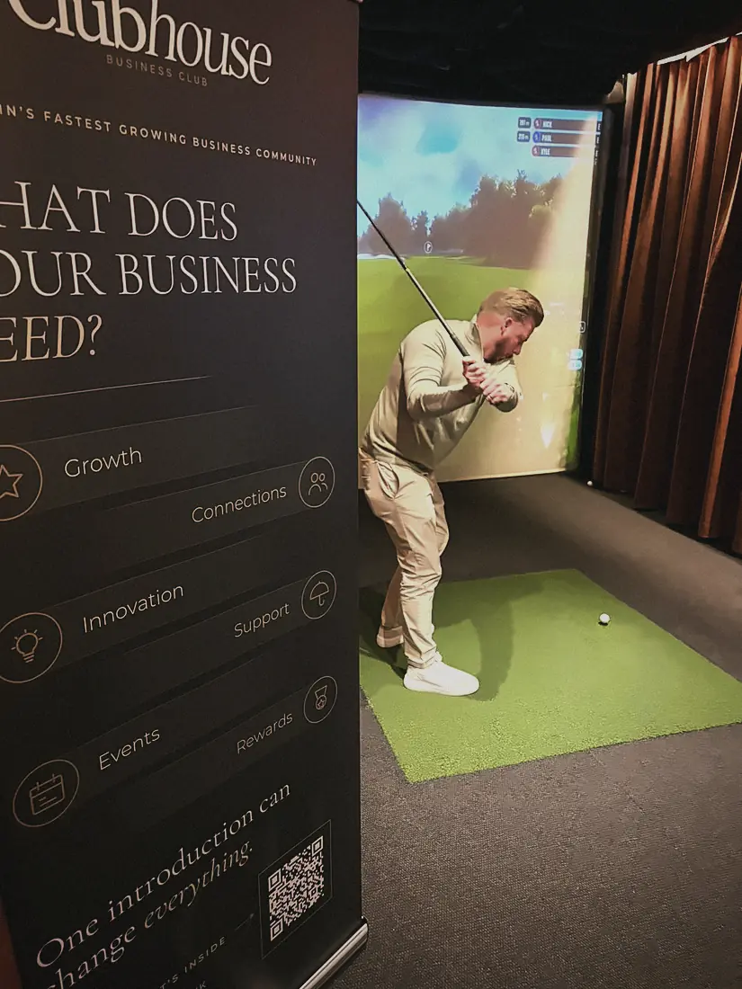 A member mid-swing on a simulator beside the Clubhouse banner at Pitch